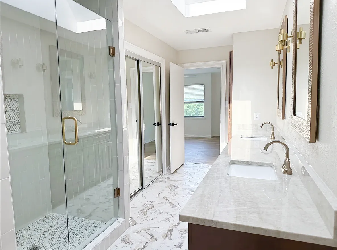 Bright remodeled primary bathroom by Fin Home with a glass shower, marble counters, and brass fixtures